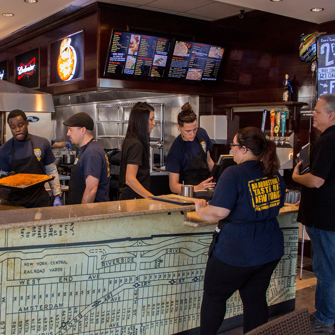 the interior of NYPD Pizza Hunter's Creek. Employees gather around the front counter.
