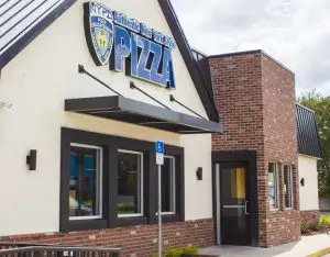 Exterior of the NYPD Pizza Apopka restaurant with white walls, black trim, and a brick entry tower.