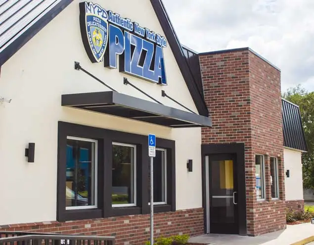 Exterior of the NYPD Pizza Apopka restaurant with white walls, black trim, and a brick entry tower.