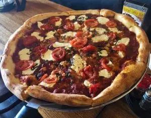 Whole pizza topped with sliced tomatoes, melted mozzarella, herbs, and a thick golden crust on a serving tray.