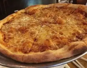 Whole cheese pizza with a golden crust and melted cheese served on a metal tray.