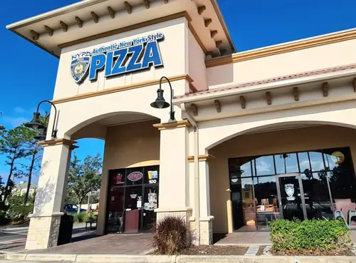 The NYPD Pizza Lake Cay restaurant with a tall arched façade, two black hanging lamps, and wide glass entry doors beneath the arches.