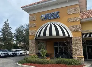 The NYPD Pizza Metro West restaurant with a yellow exterior, striped black-and-white awning, and stone accent columns at the corner.