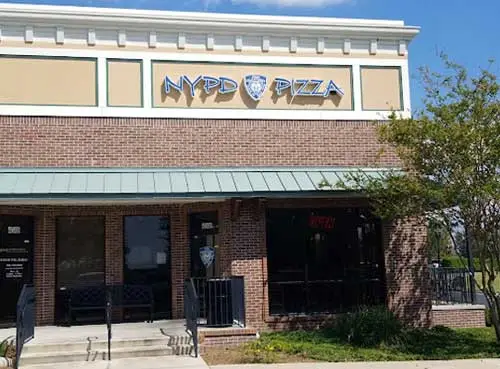 The NYPD Pizza storefront in The Villages with a brick façade, a green metal awning, and steps leading to the front entrance.